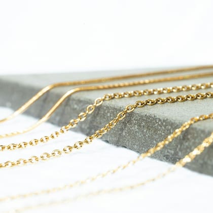 Fine gold cable chains laid across a grey stone on white
