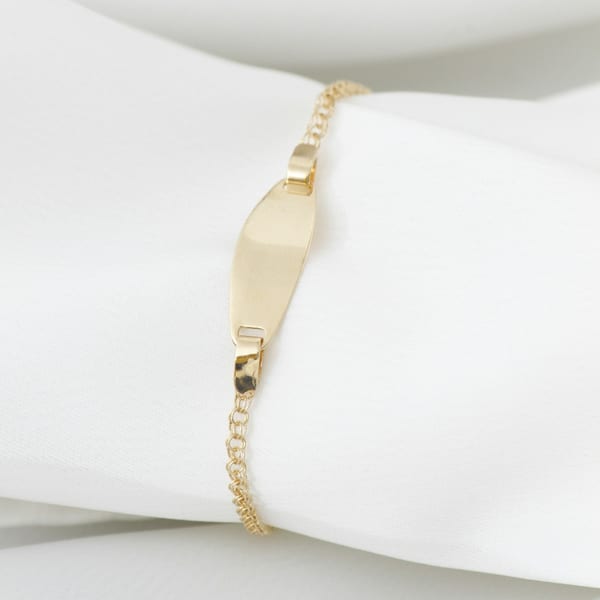 Fine gold chain bracelet with a small curved ID plate, on white cloth