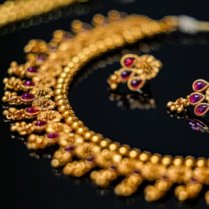 Gold bead necklace with ruby-set drops and matching earrings on a dark ground