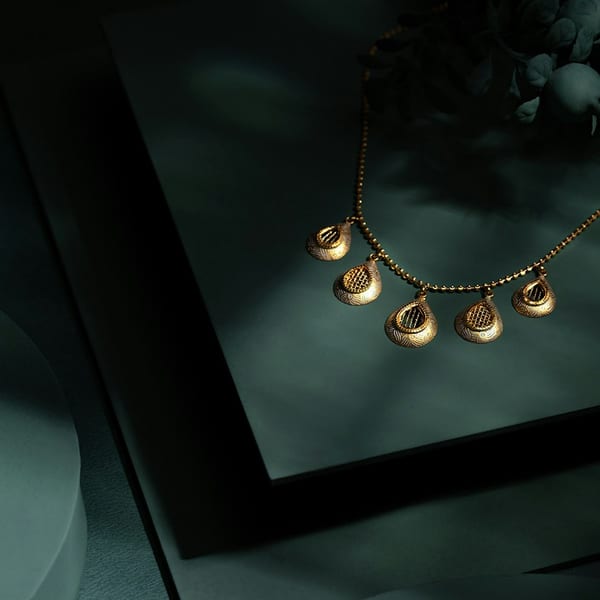 Fine gold necklace with five small petal drops on a dark slate stand
