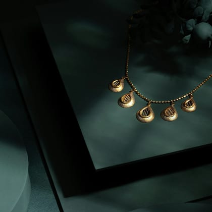 Fine gold necklace with five small petal drops on a dark slate stand