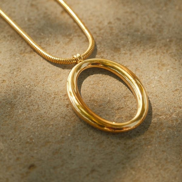 Polished gold oval loop pendant on a snake chain, on sand