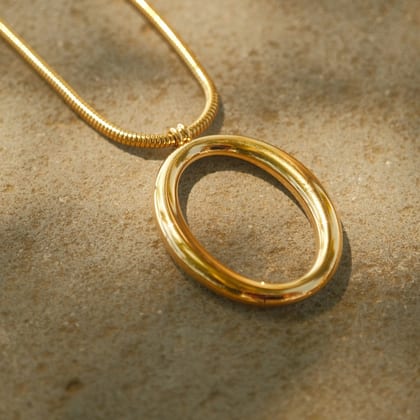 Polished gold oval loop pendant on a snake chain, on sand
