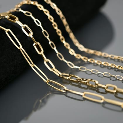 Several gold paperclip and cable chains draped over a grey stone