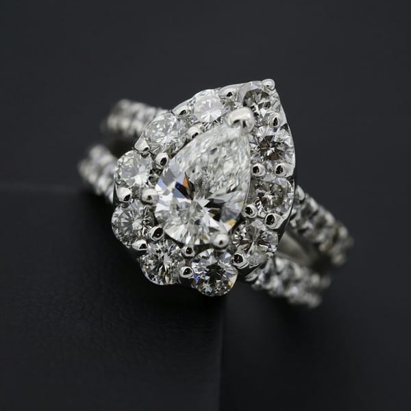 White gold ring with a large pear-cut diamond inside a cluster of round diamonds, on black