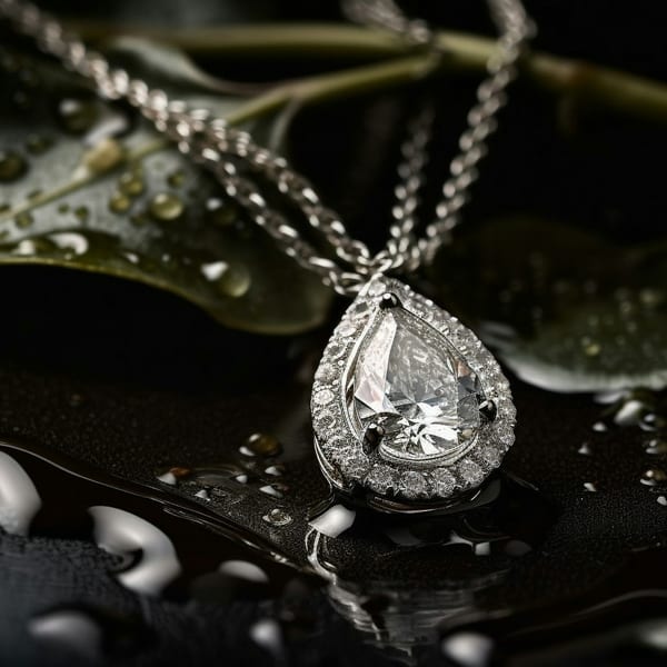 White gold pendant with a pear-cut centre stone in a diamond halo, on a dark leaf