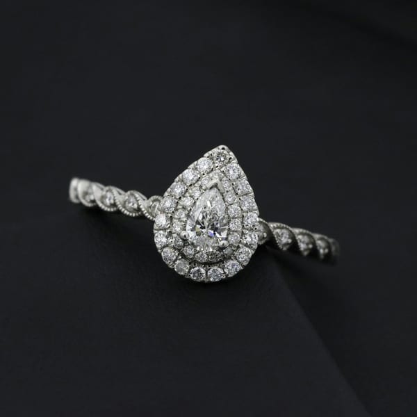 White gold ring with a pear-cut diamond in a halo, on black