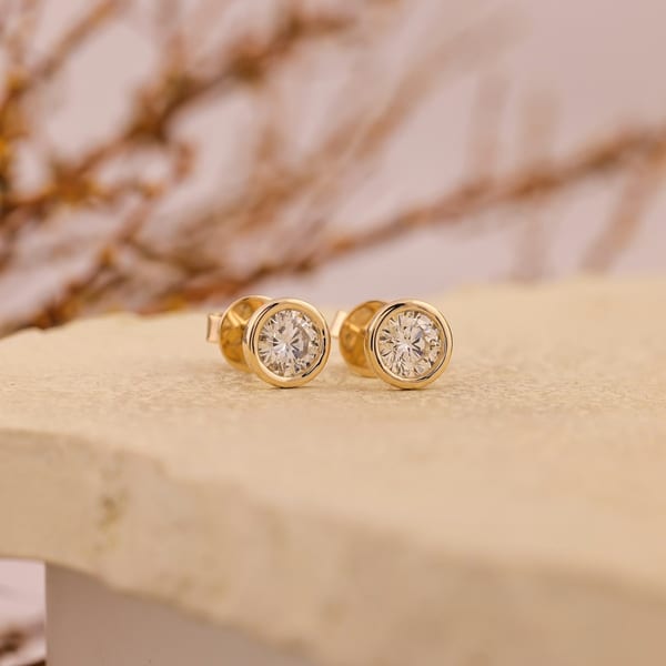 Pair of round diamond studs in yellow gold on a stone ledge