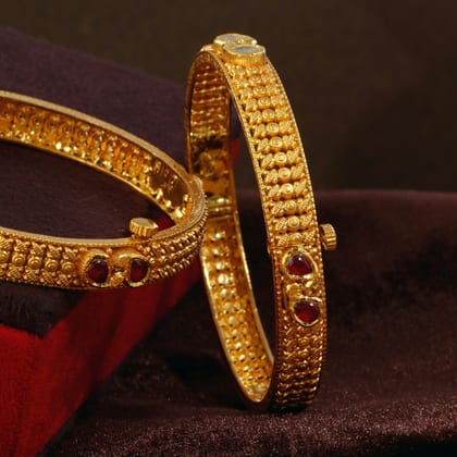 Two gold bangles with beaded rows and ruby accents on a dark velvet cushion