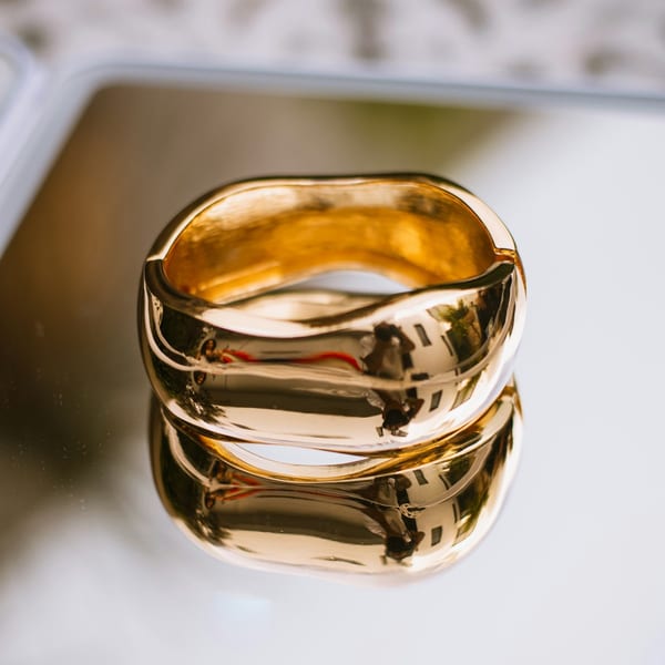 Wide polished gold band with a sculpted wave, reflected in a mirror
