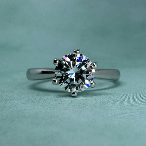 White gold solitaire ring with a round diamond in six claws, on teal