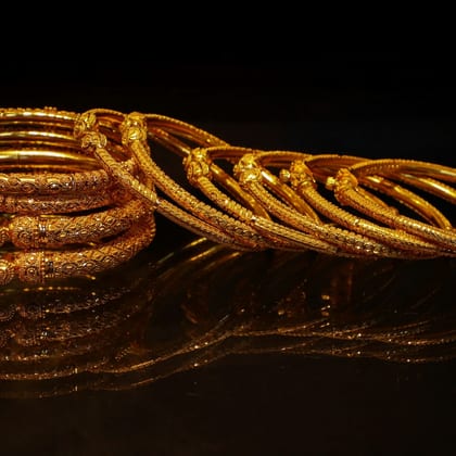 A stack of textured gold bangles reflected on a dark surface