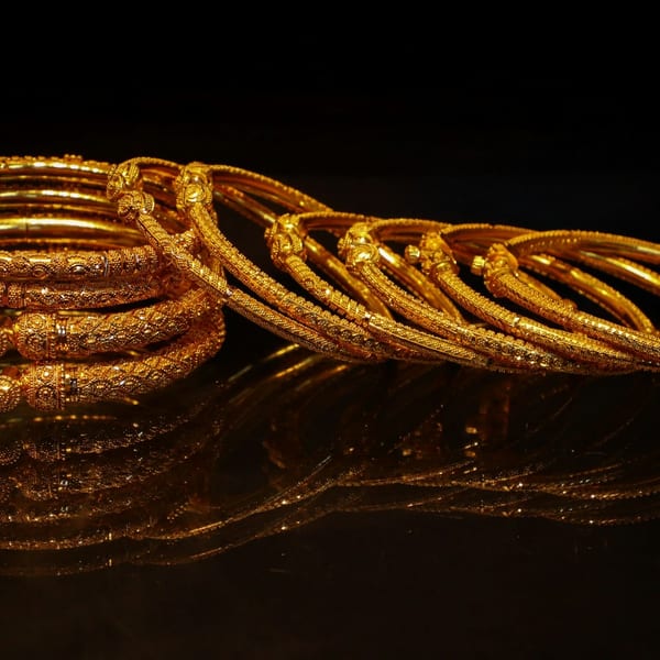 A stack of textured gold bangles reflected on a dark surface