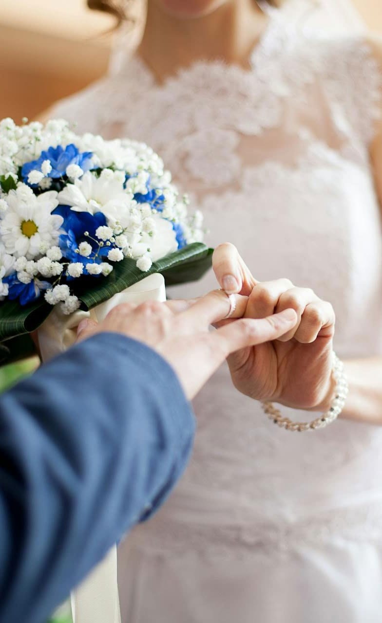 Groom placing a ring on the bride’s finger beside a blue and white bouquet